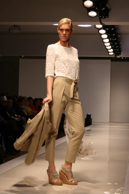 a woman walking down the runway wearing a white blouse and beige pants