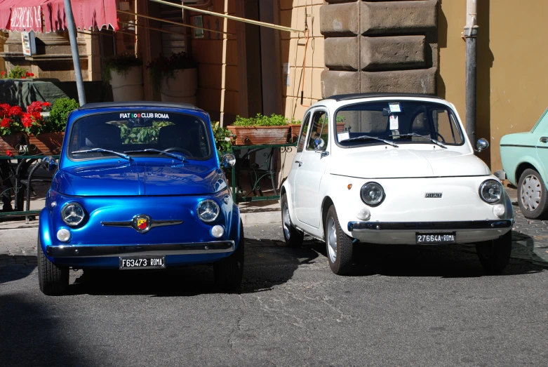 two classic cars parked in front of a tan building