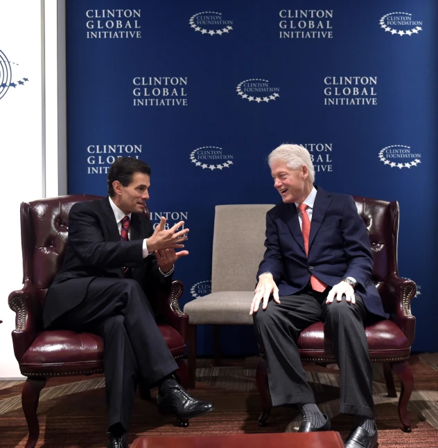 two men in suits sitting in chairs and talking