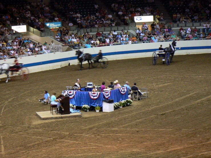 a crowd in an arena with a horse, wagon and a carriage