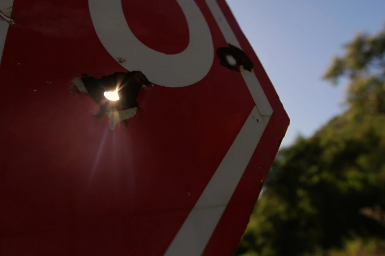 a close up of a red stop sign with the sun through a hole