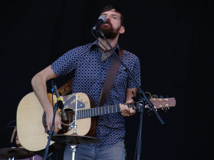 man singing into a microphone while playing an acoustic guitar