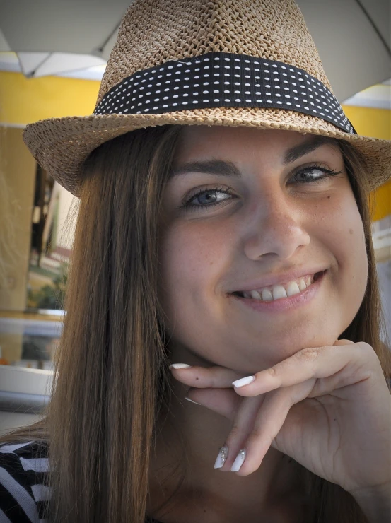 a beautiful young woman in a hat holding her hand next to her face