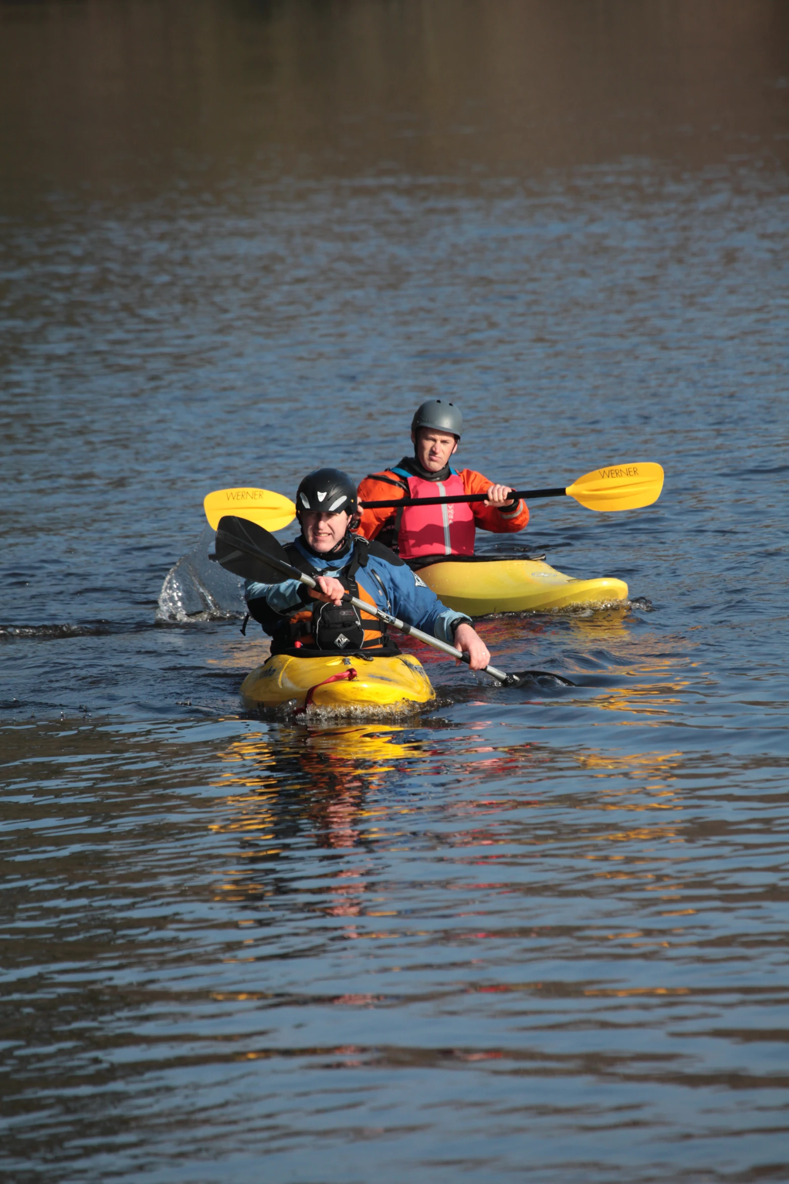 two people paddling in kayaks on calm waters