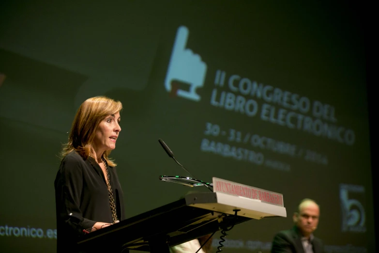 a woman in a suit and tie stands at a podium while looking out to her left