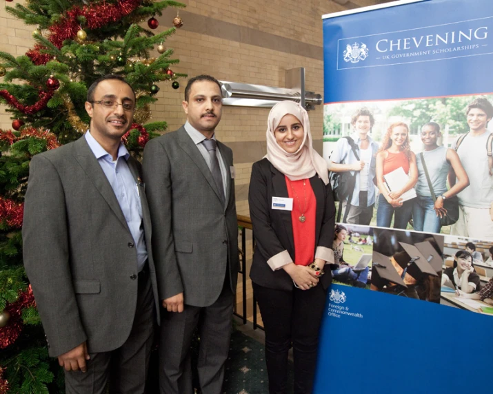 three people standing beside a poster by a christmas tree