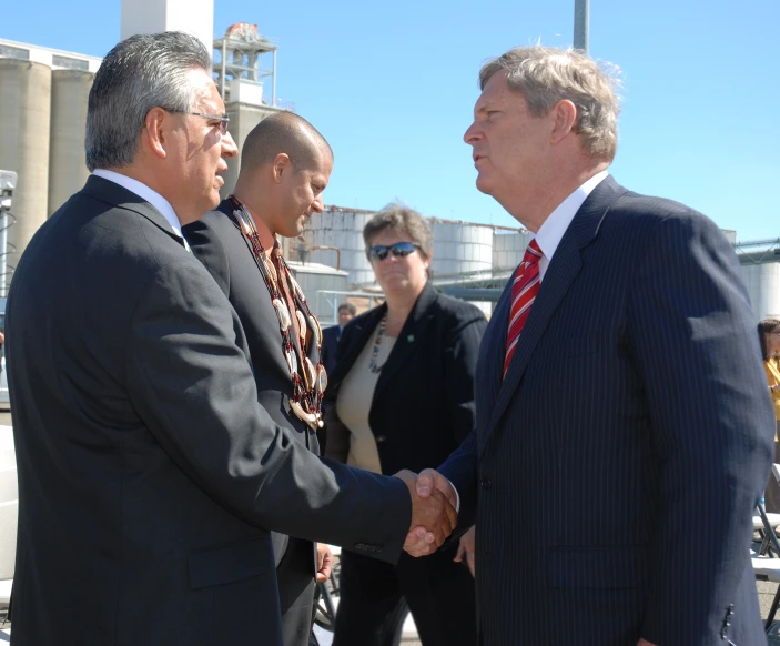 two men shaking hands with other people near by