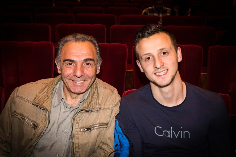 two men sitting in front of a theatre chair