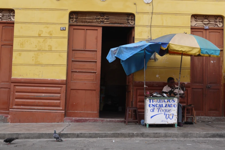 a man sitting at a table underneath an umbrella next to a store