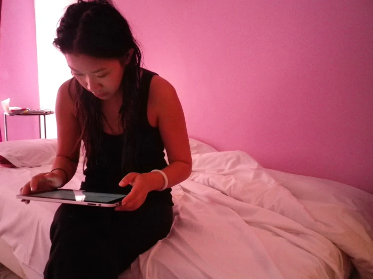 a woman sitting in a bed looking at an electronic device