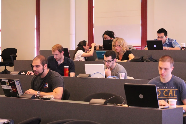 a group of people sitting in a classroom using laptops