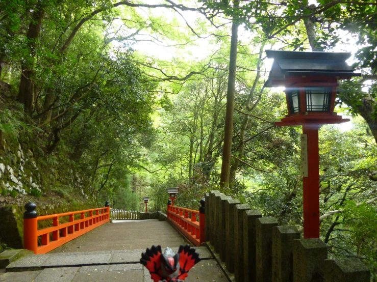 a long red bridge surrounded by greenery on the other side of a narrow pathway