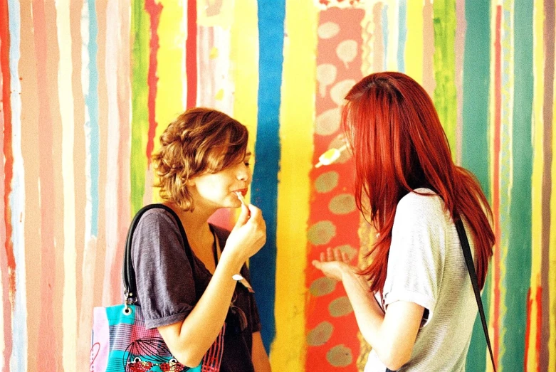 two women in front of colorful wall looking at their cell phones