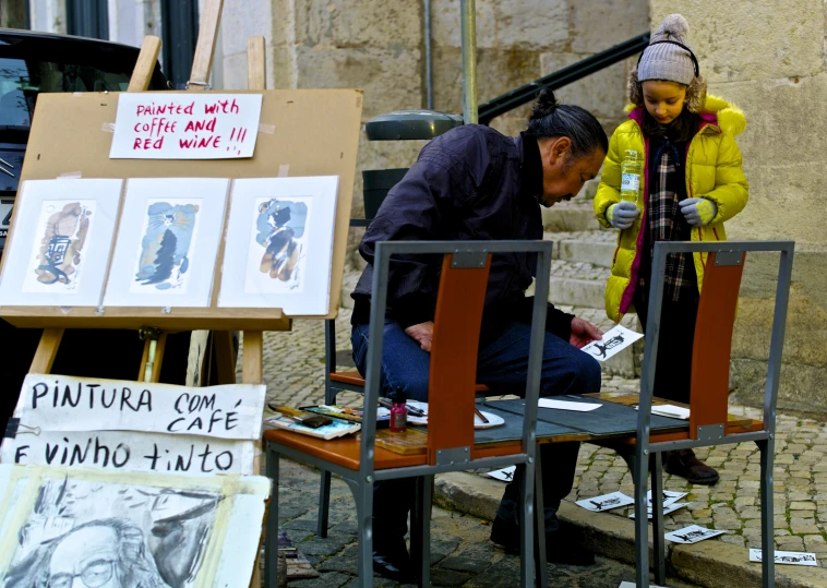 man in brown jacket looking down at drawings on an easel