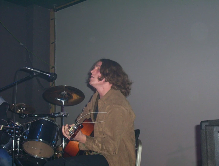 a person playing a guitar in a room with a microphone and drums