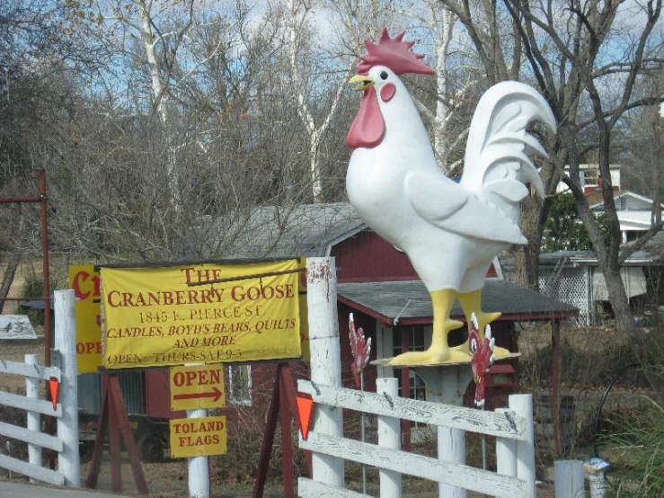 a large statue of a rooster is posed on a fence near a building