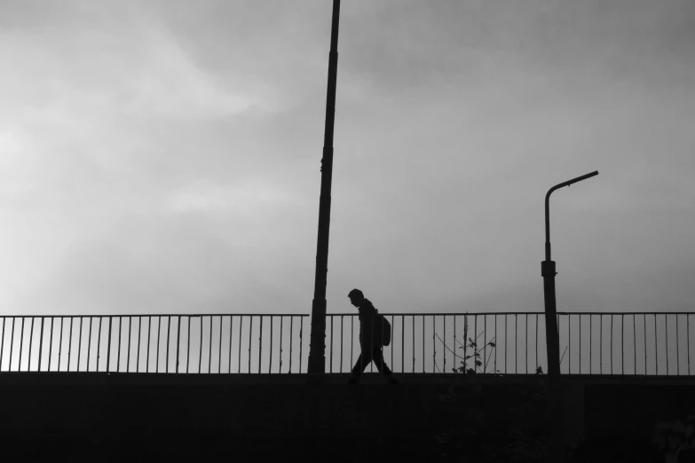 a man walking over a bridge under a light pole