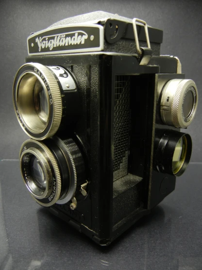 an old camera with three lenses on a black table