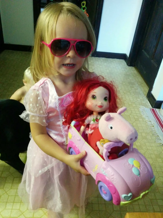 a little girl in sunglasses is holding a doll and horse toy