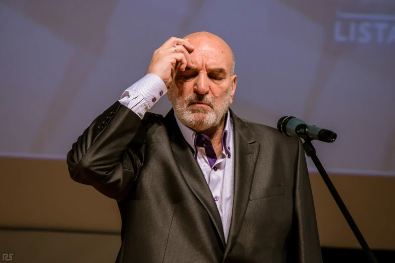 man in suit and tie holds his head above his ear