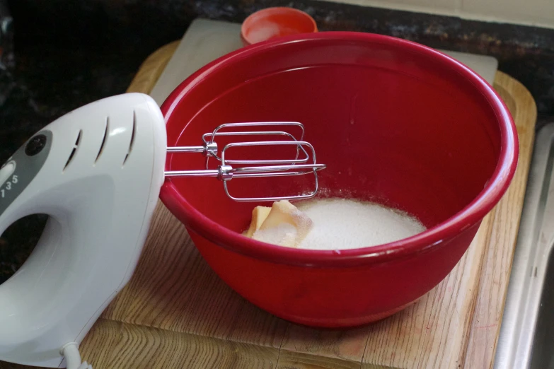 red bowl on a wooden  board next to white mixer