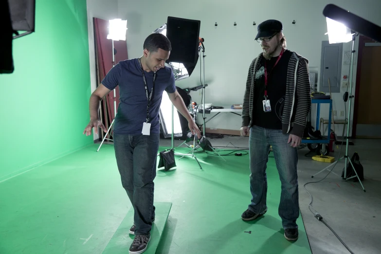 two young men are standing in a room in front of green screen