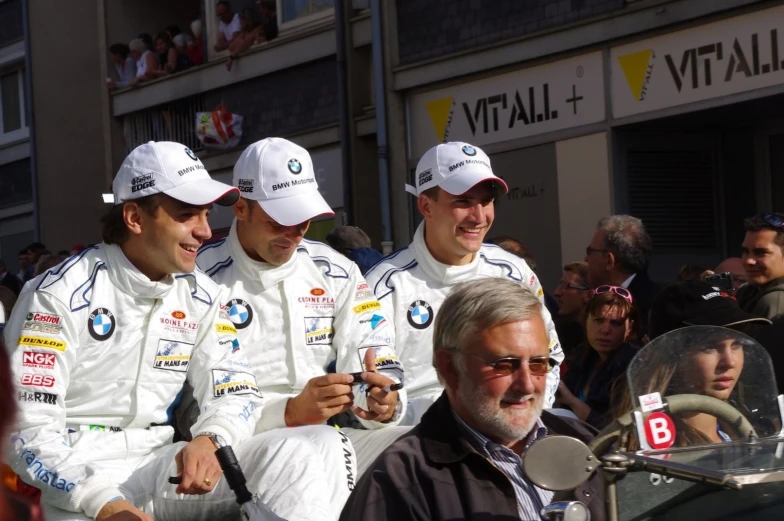 three men in racing uniforms with hats talking to each other