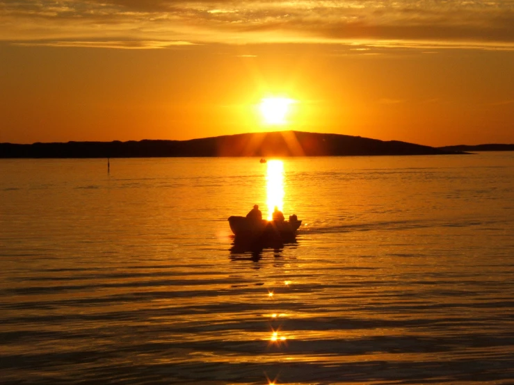 two people sitting in a small boat in the water at sunset