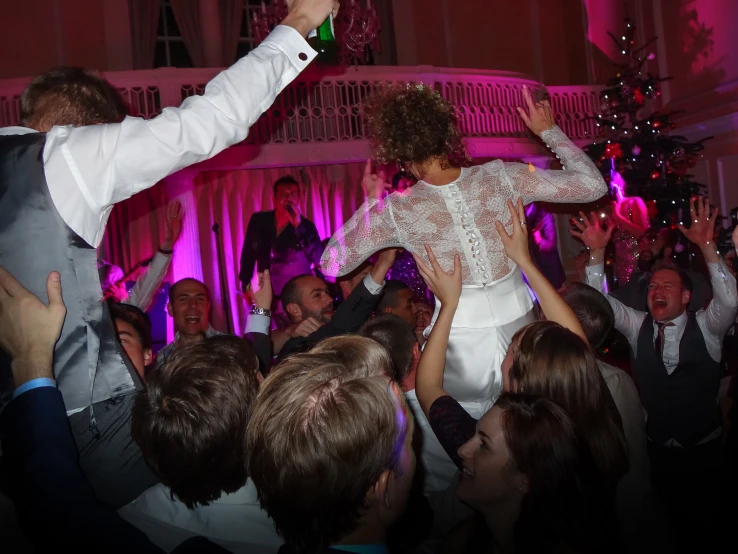 a couple in wedding dresses standing in a room filled with people