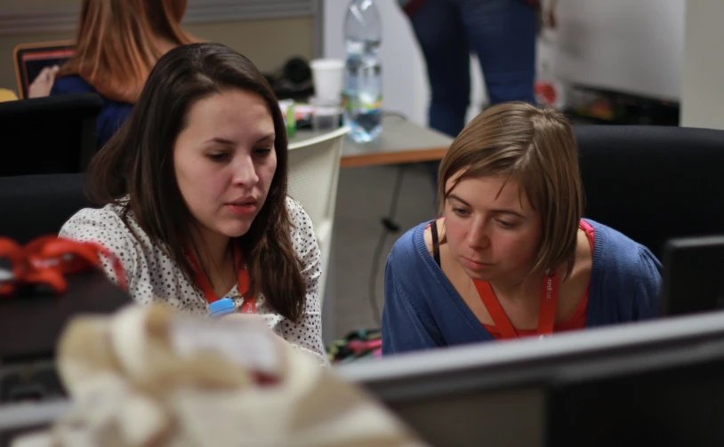 two women sitting in front of computers with one working on a small screen