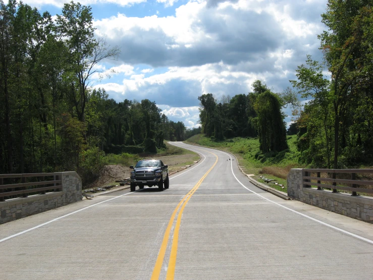 a black truck driving down a road with tall trees