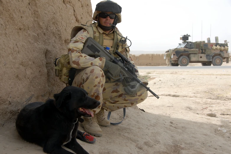 a soldier squatting down and his dog sits beside him