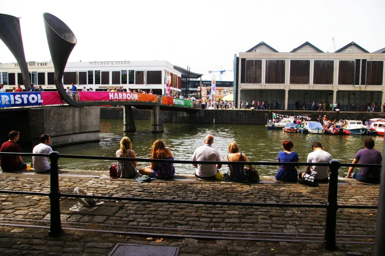 people are sitting on the side of the water watching boats go down