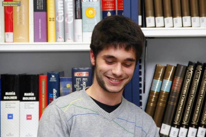 a man smiles as he stands in front of a bookshelf with his eyes closed