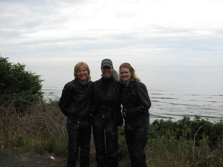 three smiling friends posing in front of the ocean