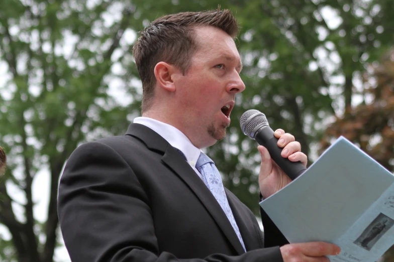 a man standing in front of a microphone with an open book in his hand