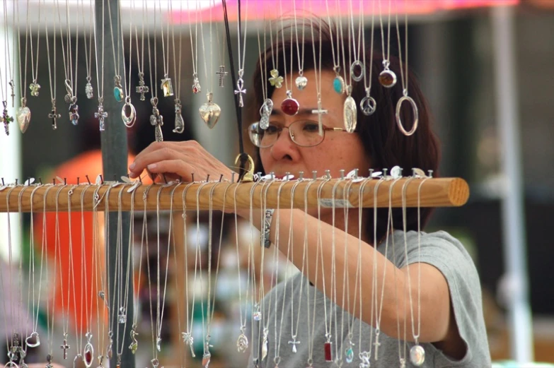 a woman weaving on an umbrella string with lots of earrings