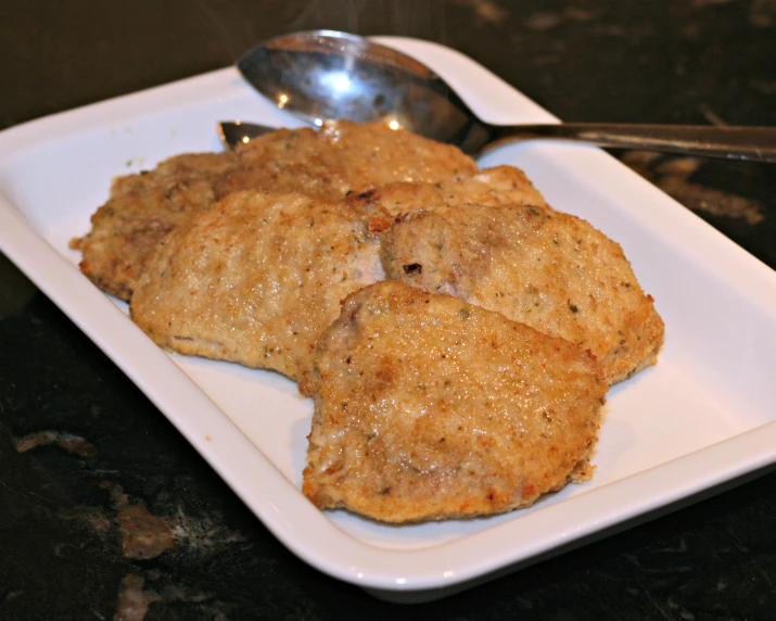 a square white plate with three pieces of bread and two spoons