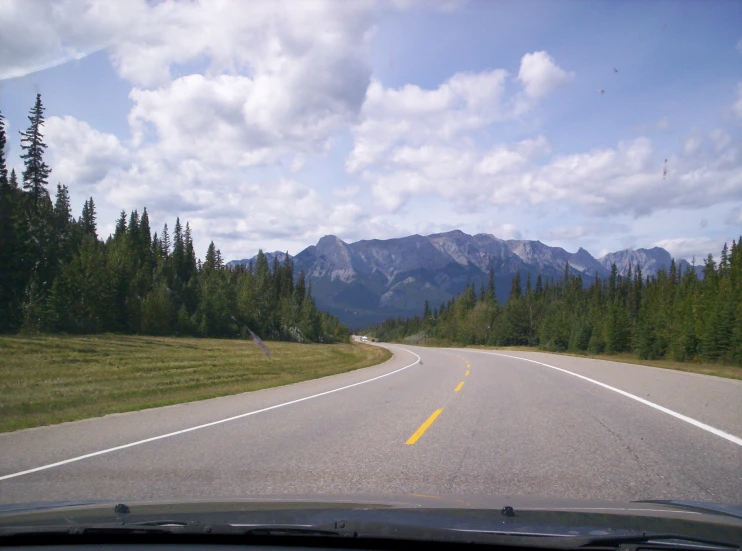 an open road leading to the mountains with clouds above