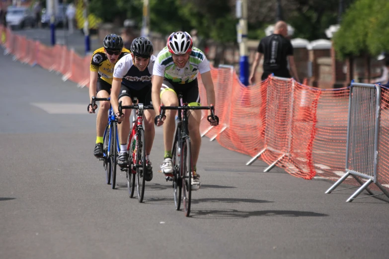 three people on bicycles riding next to orange barricades