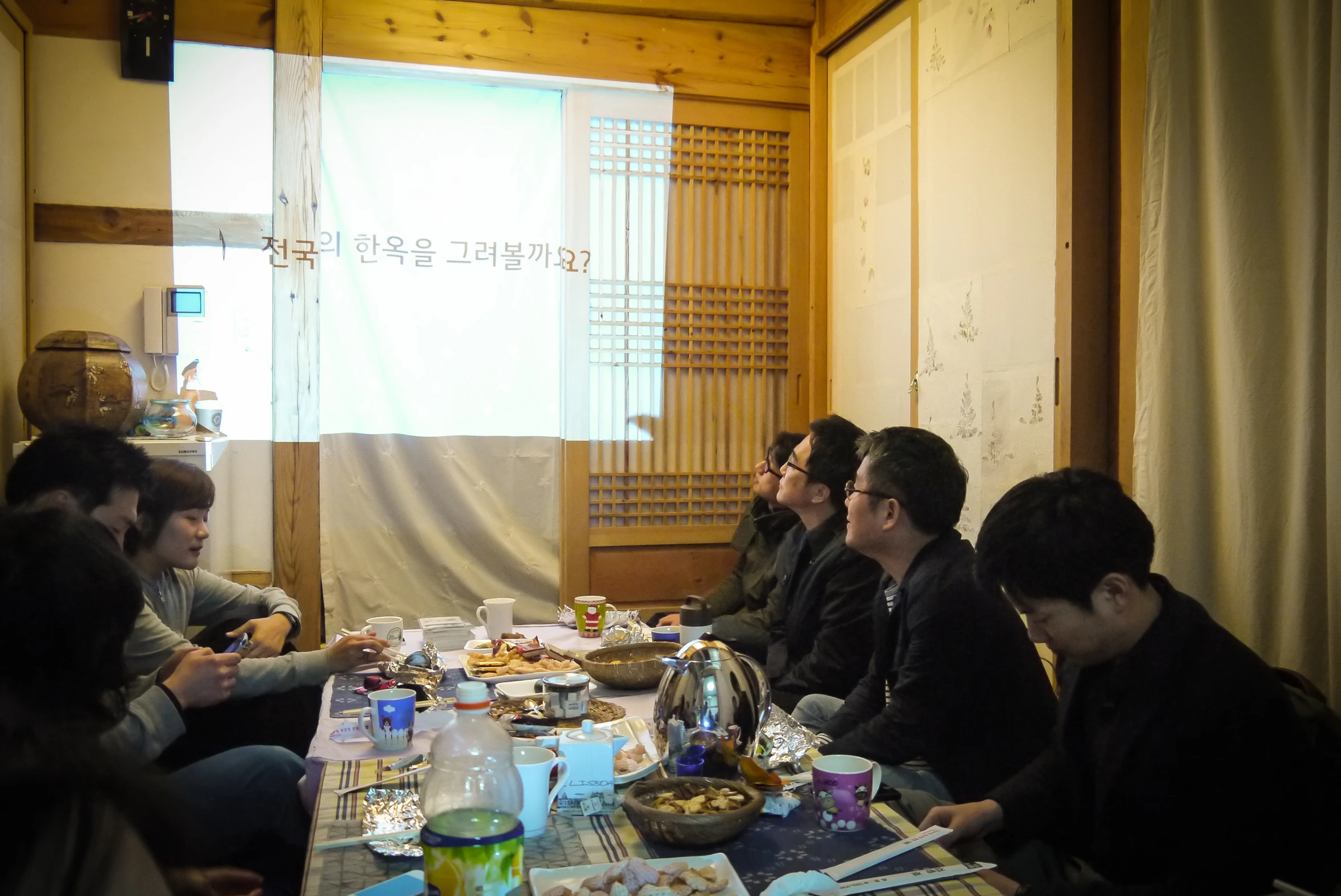 five people sitting at a long table with papers and food on them