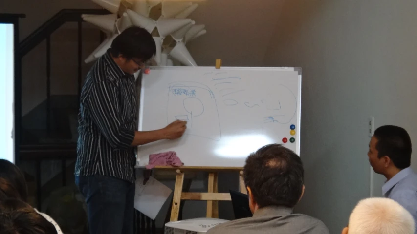 a group of people sitting around a white board with some writing on it