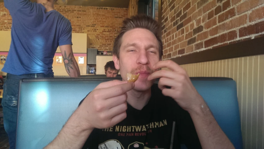 there is a man sitting in a restaurant taking a bite out of his spoon