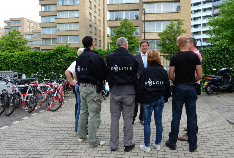 four people wearing police vests standing on a brick walkway with bicycles in the background