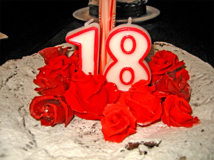 red and white rose covered cake with candles in the shape of the number eighteen