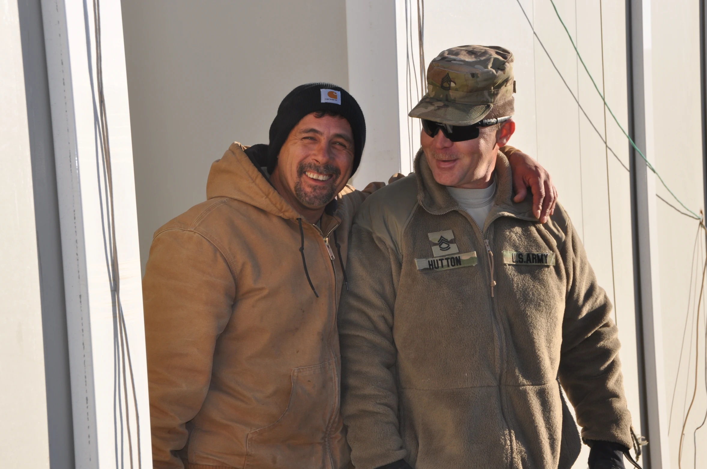 two men are standing by the building wearing coats