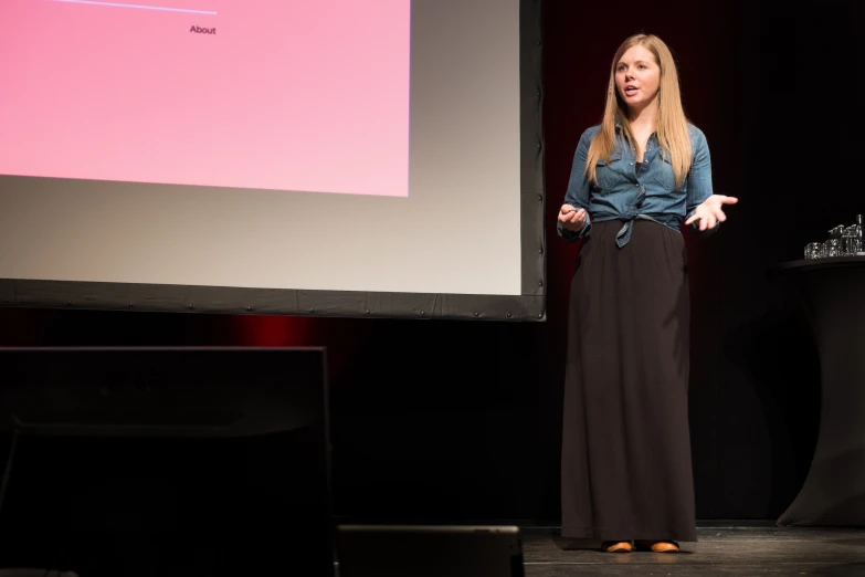 a woman stands in front of a screen at the start of a conference