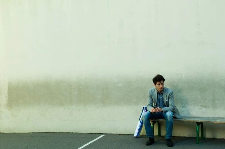 a person sitting on a bench in front of a white wall