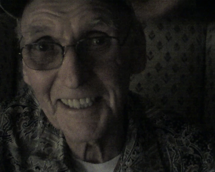 an elderly man with glasses and a hat smiling