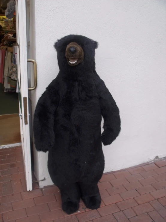 a large black teddy bear sitting next to a door